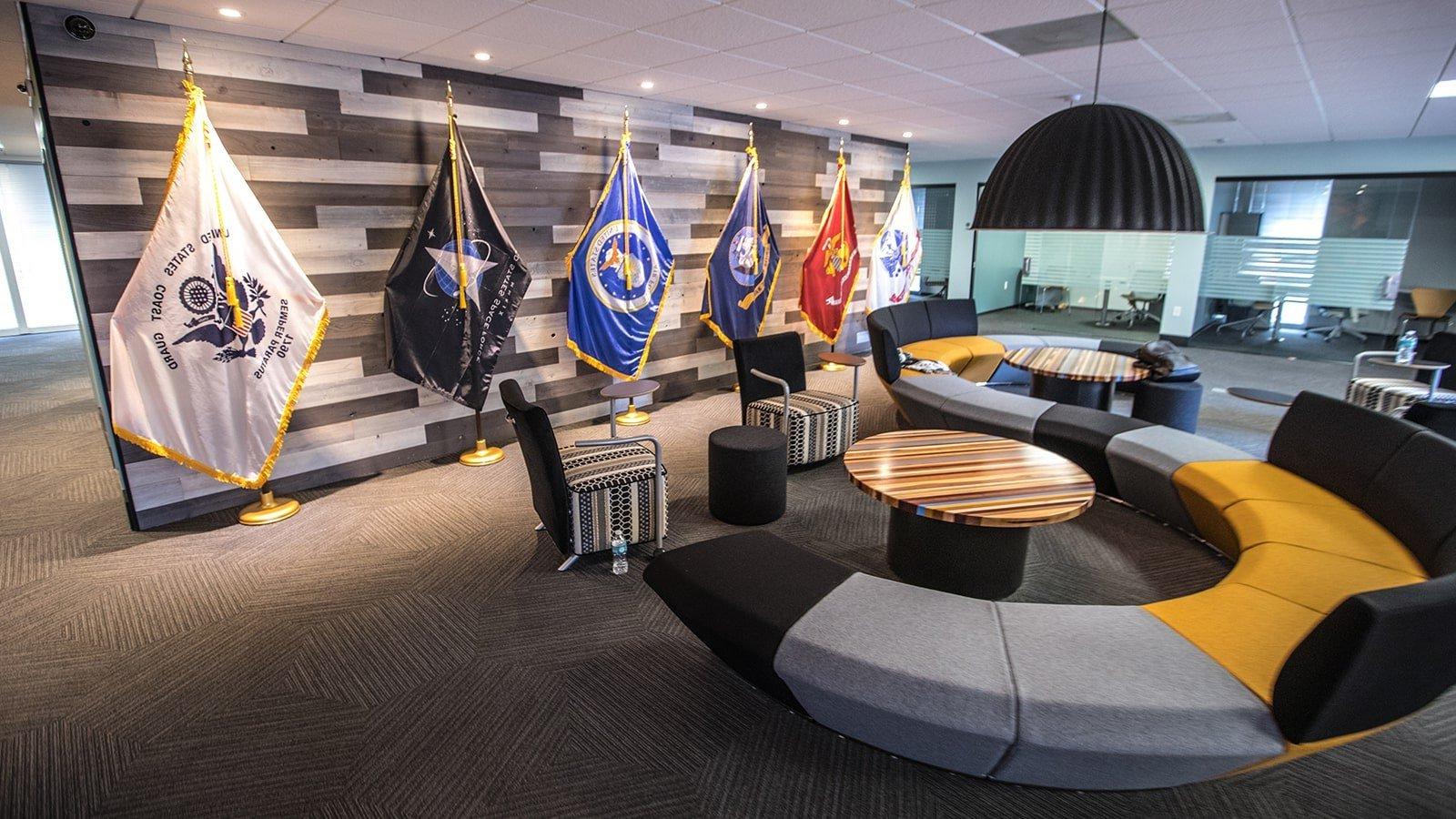An image of Full Sail’s Military Student Success center shows a large couch, small meeting rooms, and flags representing each branch of the US Armed Services.