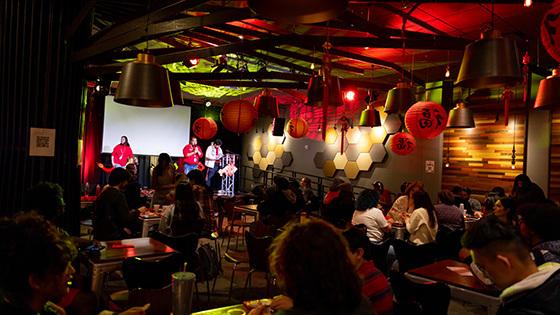 一群人聚集在Full Sail的树屋，客人们坐下来，主持人在舞台上. 房间里灯光昏暗，装饰着农历新年的红纸灯笼.
