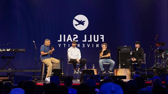 MLB Pitcher Adam Wainwright and three other people are seated on a stage during a panel, the large-scale LED screen behind them reads “满帆大学” against a blue backdrop.