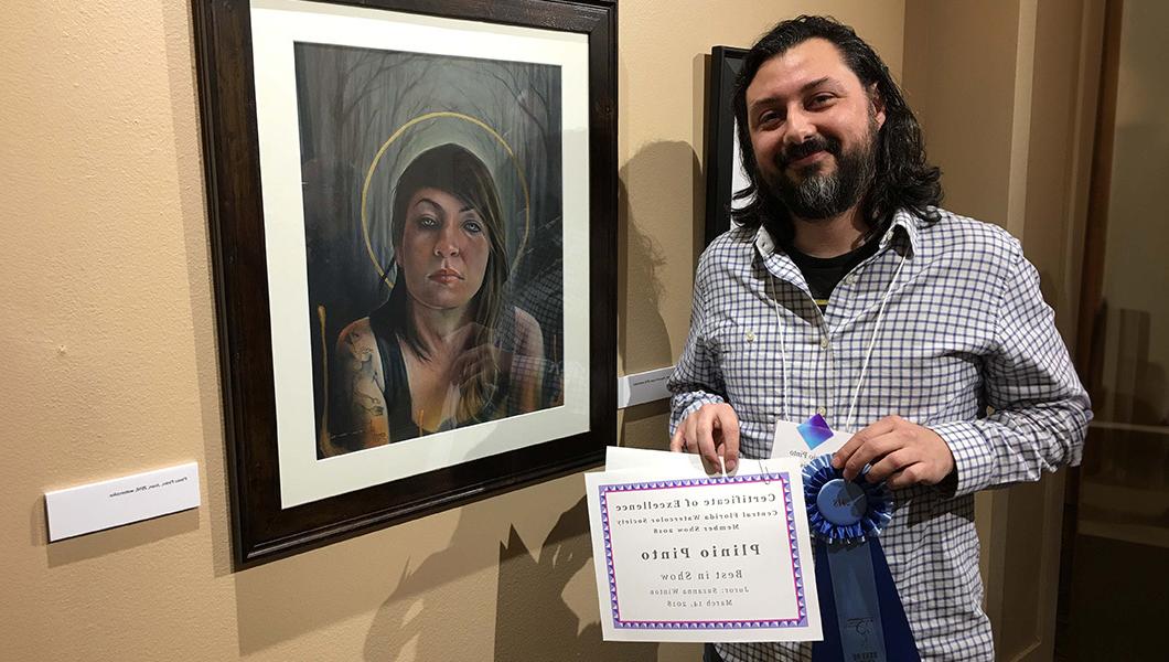 A smiling man stands next to a watercolor portrait of a woman. He is holding a blue ribbon and a Best in Show certificate.